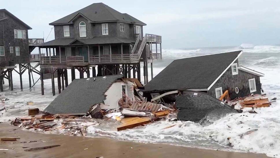 A collapsed home in the high tide as two houses on stilts stand in the background