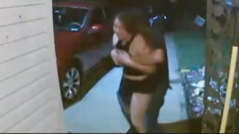 Security camera footage of woman screaming, a man has her in a bear hug and pulls her back