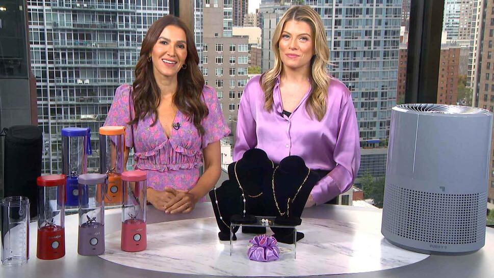 Two women standing behind a table displaying Blenders, Jewelry Set, Air Purifier