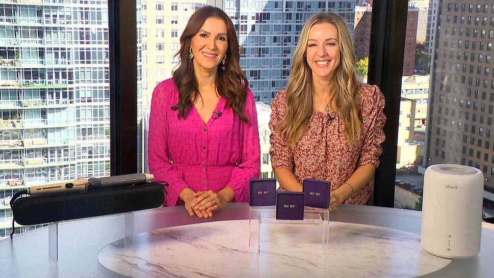 Two women standing behind a table displaying Curling Wand, Earrings, Humidifier & Diffuser