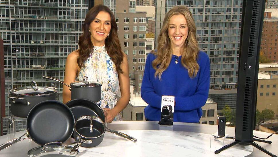 Two women standing behind a table displaying a Cookware Set, Smartwatch, Fan