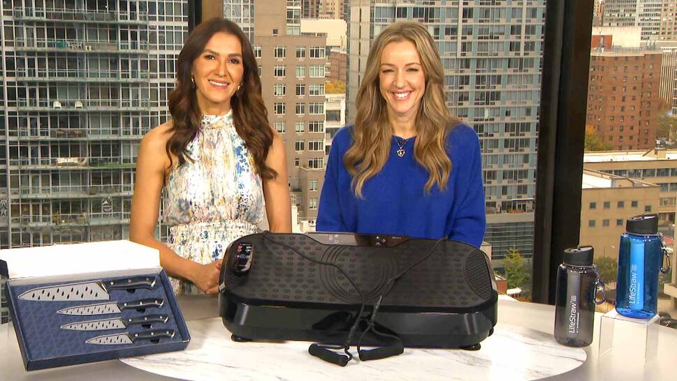 Two women standing behind a table displaying a Cutlery Set, Vibration Machine, Water Bottles