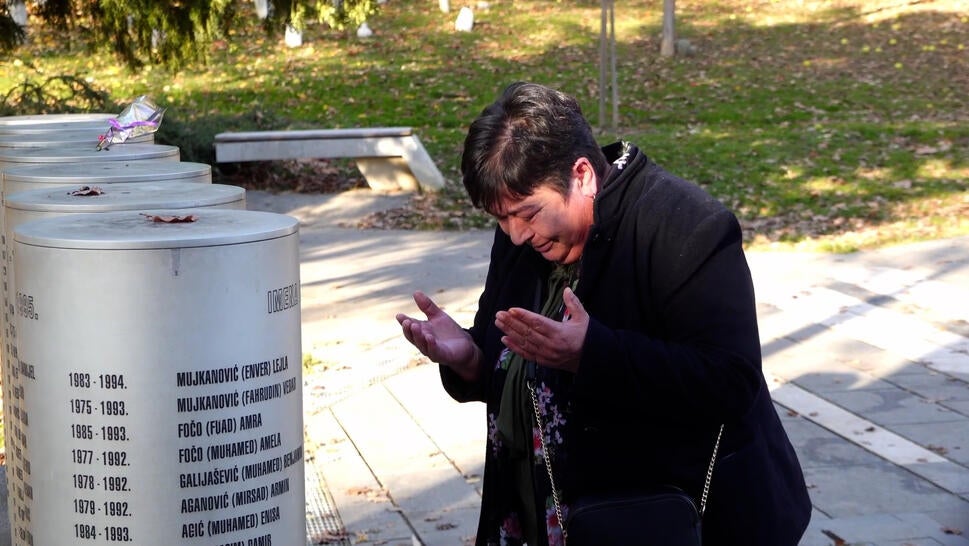 Fatima Popovac, a middle-aged white woman, kneels before memorial, in tears