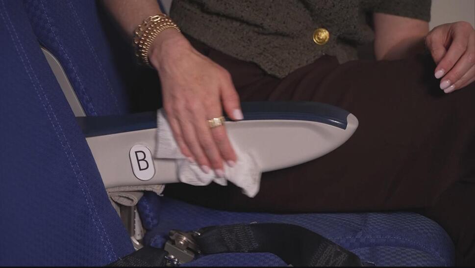 Woman's hand wiping down a plane seat arm rest