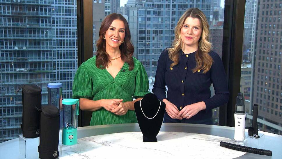 Two women standing behind a table displaying a Portable Blenders, Tennis Necklace, Cordless Vacuum