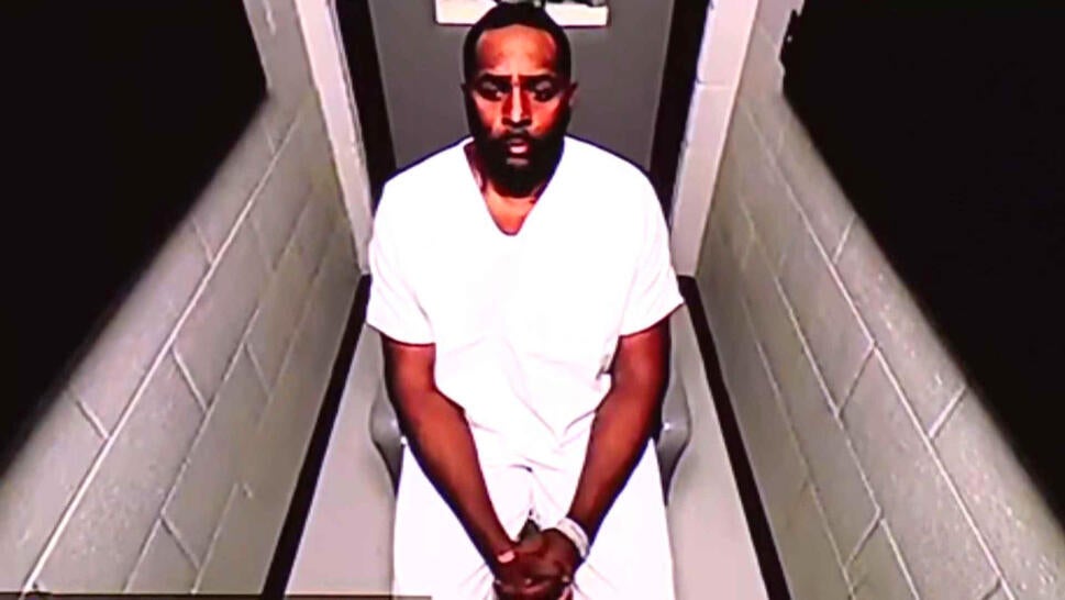 Sherrone Moore in a white jumpsuit wearing cuff as he appears virtually for court