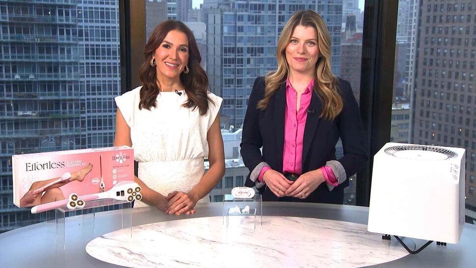 Two women standing behind a table displaying a Shaving Kit, Earbuds, Air Purifier