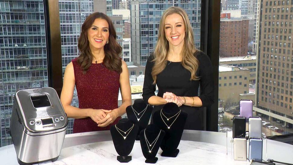 Two women standing behind a table displaying a Bread Maker, Necklace, Power Bank