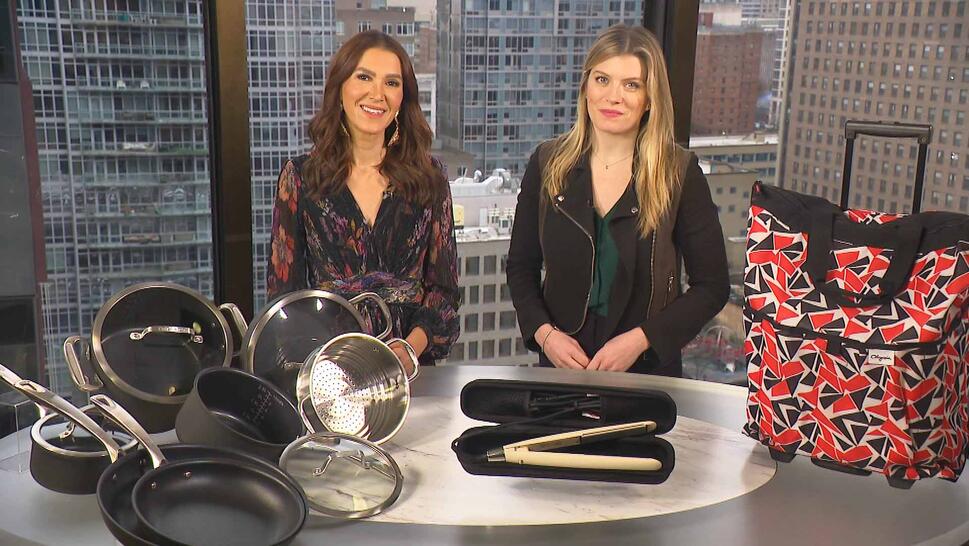 Two women standing behind a table displaying a Cookware Set, Flat Iron, Carry-On Luggage