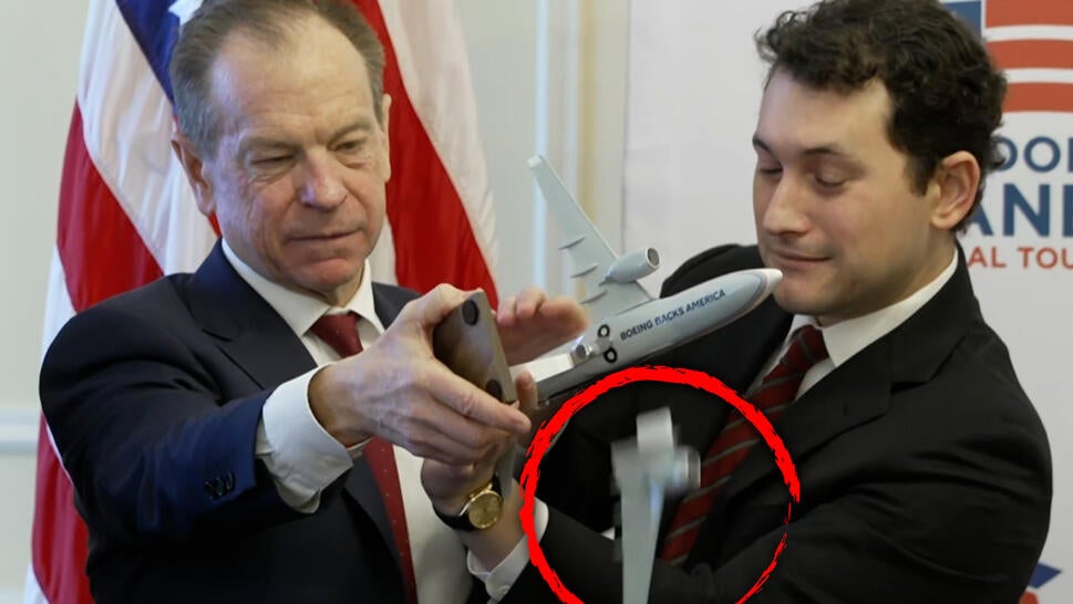 Two men holding a model of a plane as the wing falls off