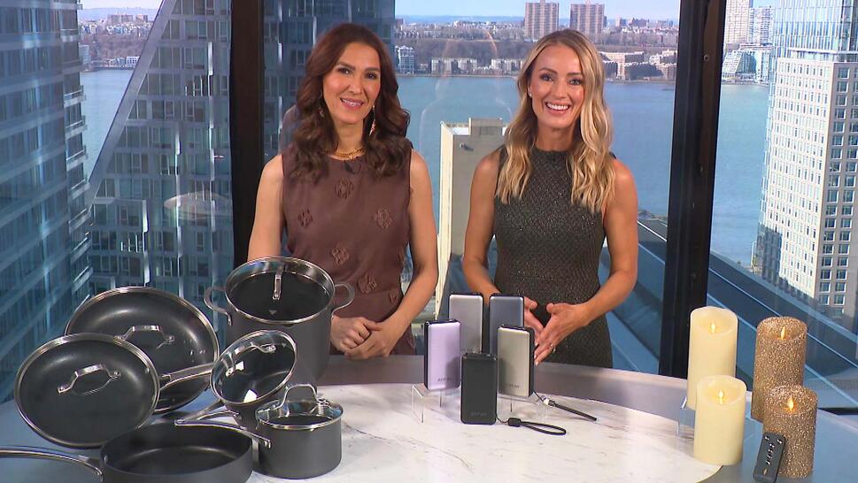 Two women standing behind a table displaying a Cookware Set, Power Bank, Candles