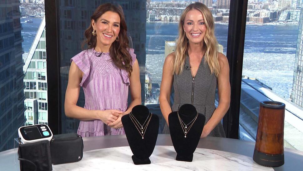 Two women standing behind a table displaying a Blood Pressure Monitor, Necklace, Humidifier