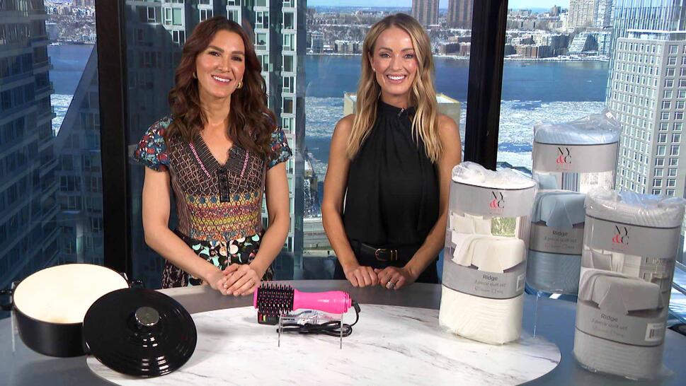 Two women standing behind a table displaying a Dutch Oven, Volumizing Brush, Quilt Set