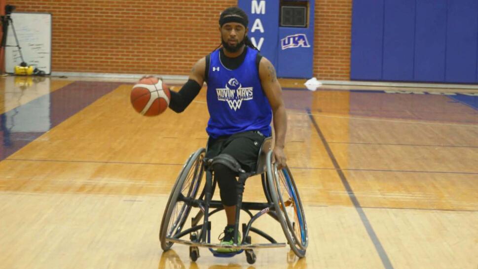 Michael Collins dribbling a basketball down a basketball court while in a wheelchair