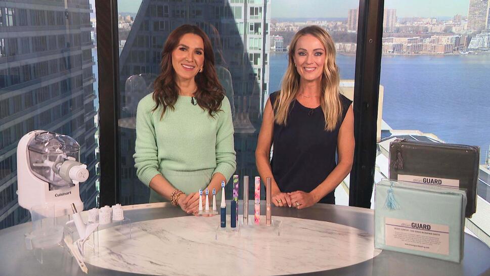 Two women standing behind a table displaying a Dough Maker, Toothbrushes, Sheet Set
