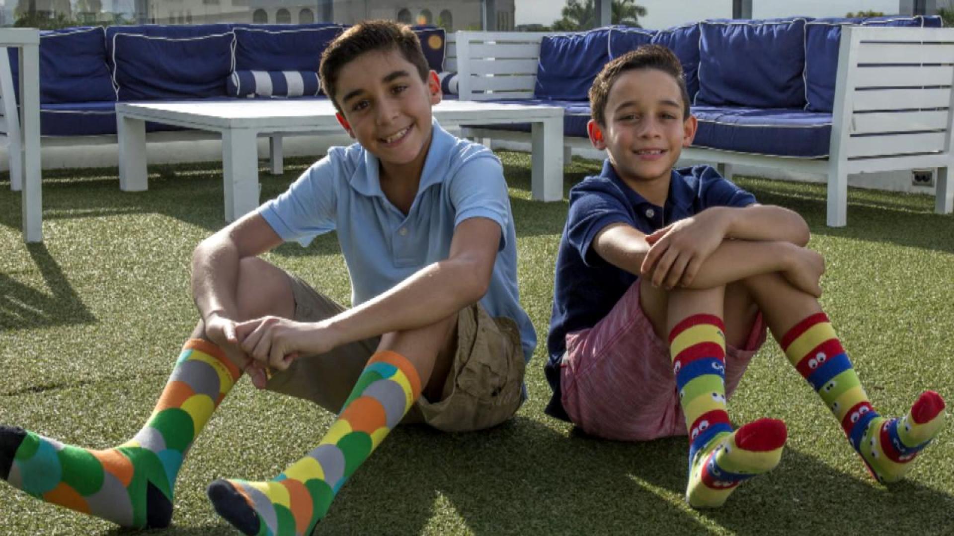 Sebastian and his brother Brandon sitting on the ground back to back, wearing pairs of their own socks.