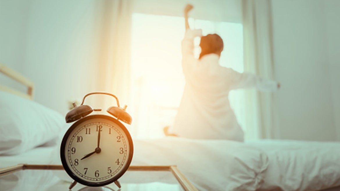 A stock image of an alarm clock and person getting out of bed. 