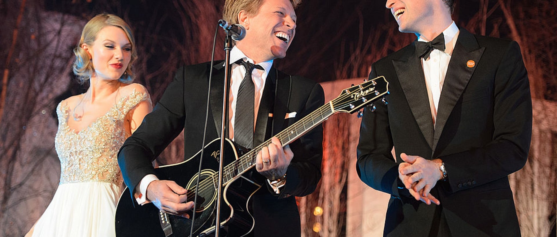 Taylor Swift, Bon Jovi holding a guitar, and Prince William - all on stage smiling