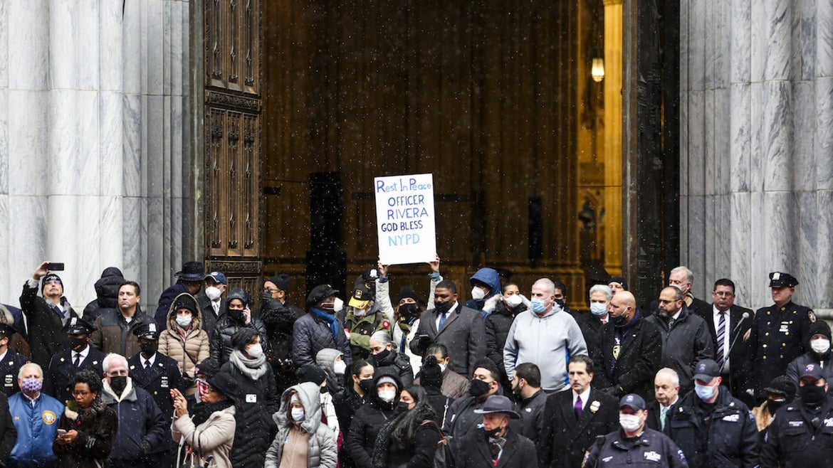 JANUARY 28: A woman with a banner walks out of the cathedral alongside thousands of police officers from different states who gather at St. Patrick's Cathedral to attend the funeral of fallen NYPD officer Jason Rivera on January 28, 2022 in New York City.