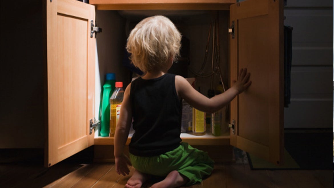 A stock image of a little boy opening cupboard of cleaning products 