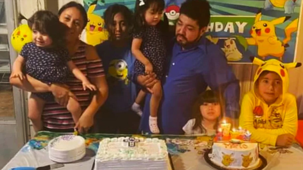 All 7 family members standing around a table with a cake on it