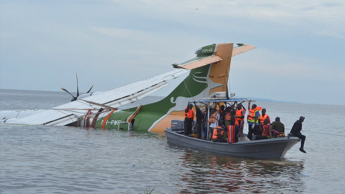 Plane partially submerged underwater next to safety boat carrying people in orange life vests