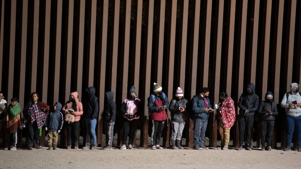Asylum-seekers line up to be processed by US Customs and Border Patrol agents at a gap in the US-Mexico border fence near Somerton, Arizona